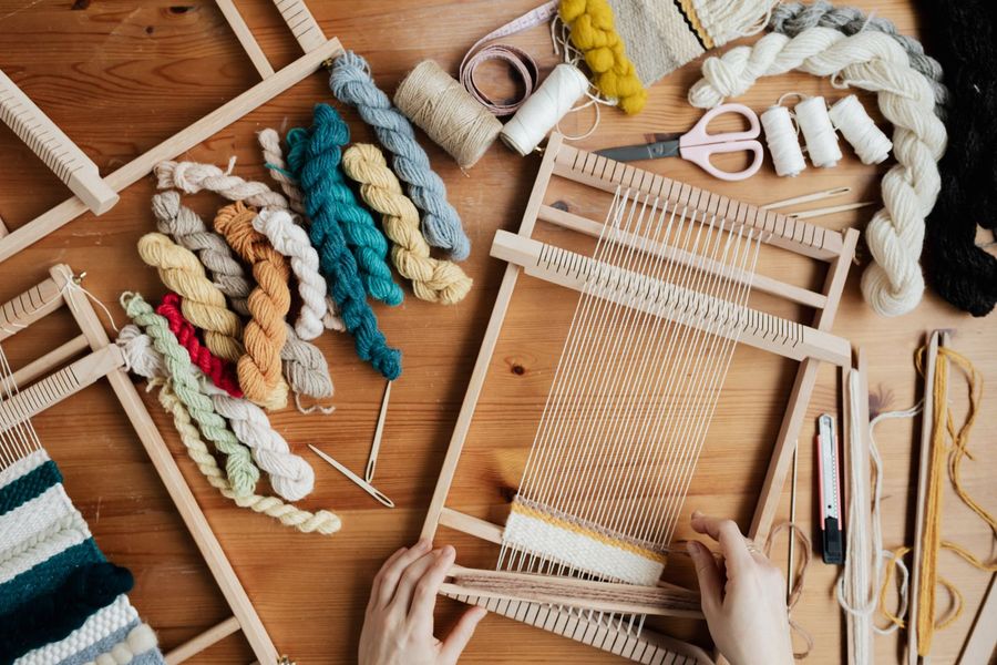 Hands weaving colourful yarn on a loom